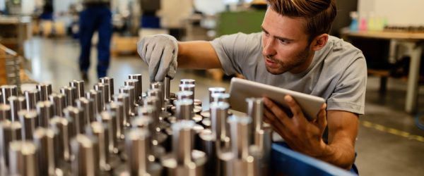 Young metal worker using touchpad while examining steel rods in a factory before the distribution.